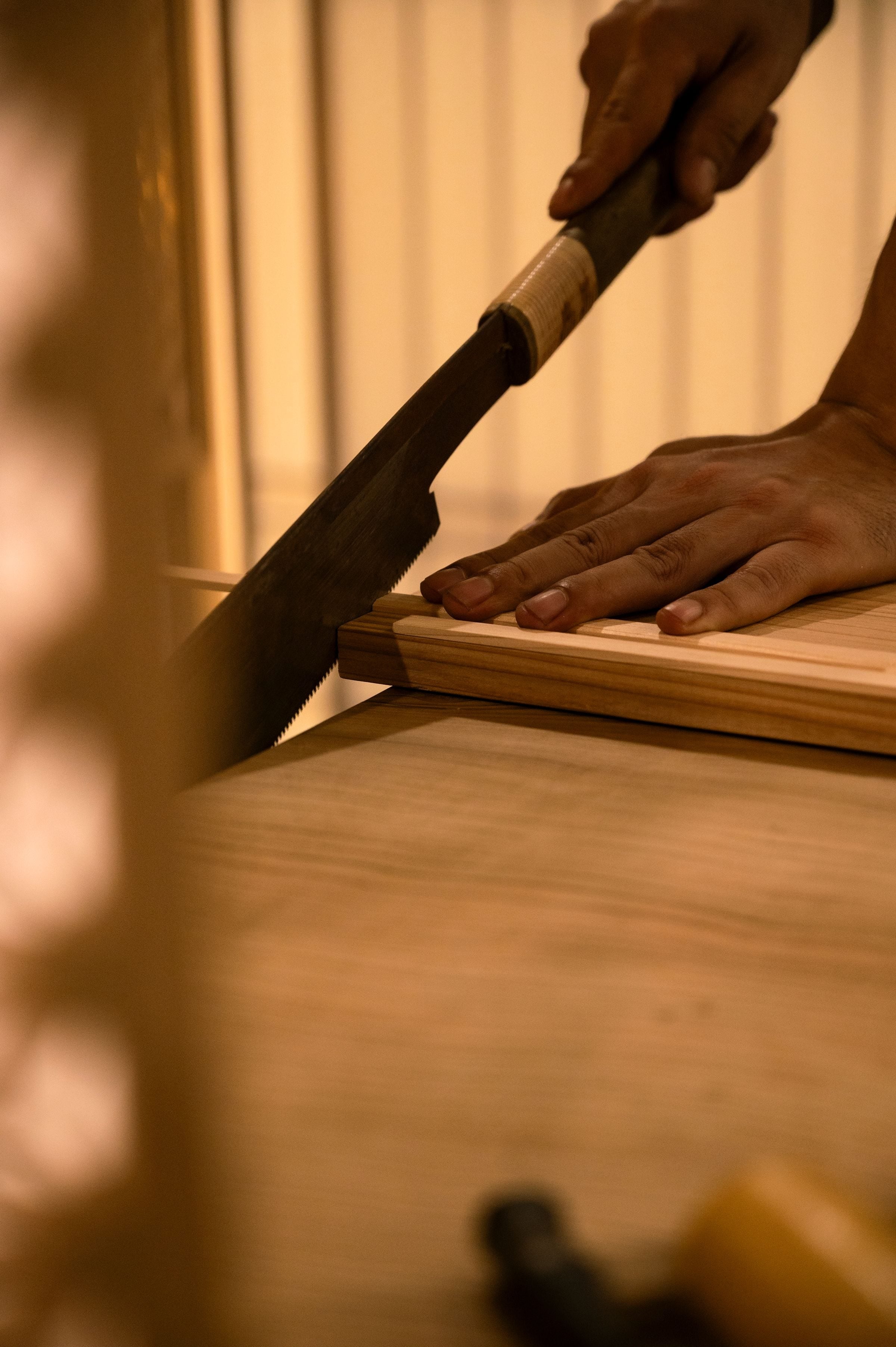 A craftsman uses a saw to cut wood indoors, highlighting fine woodworking skills.