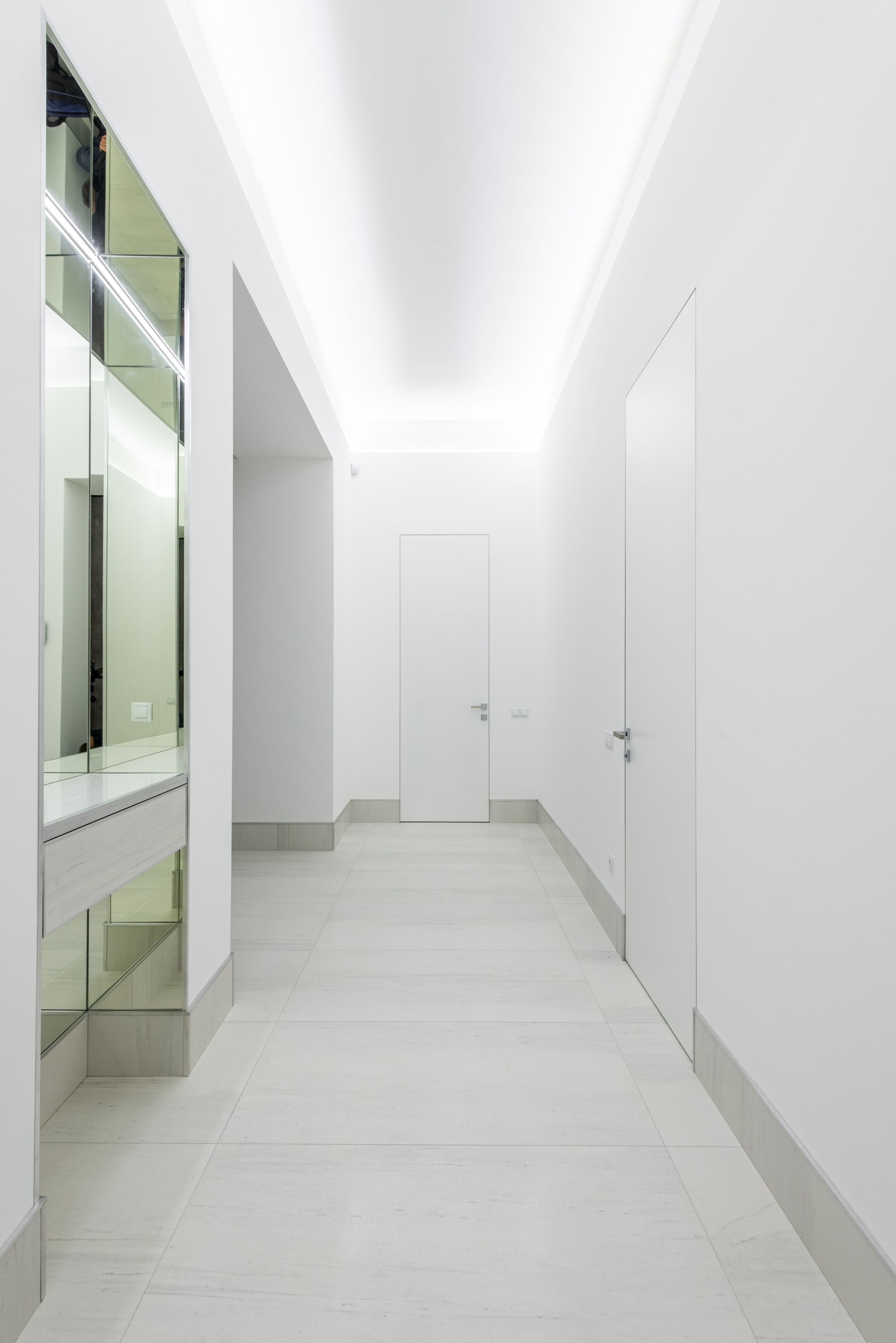 Long narrow brightly lit corridor with glass reflective surface and white doors at home with stylish design and glowing lights