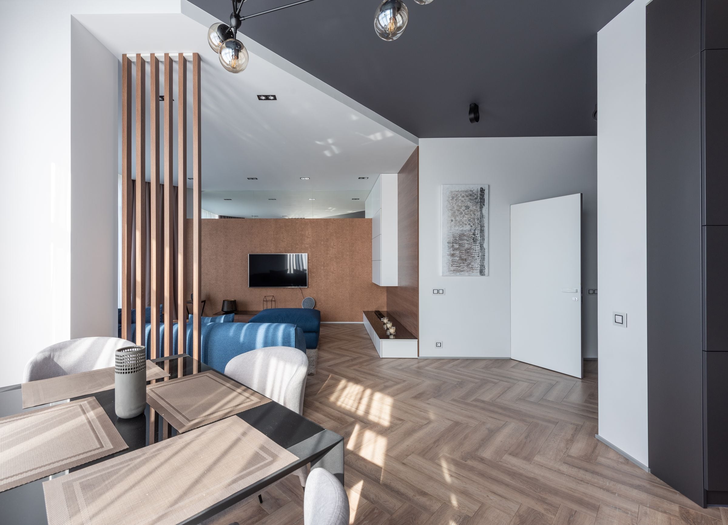 Interior of spacious flat with chairs at table placed near living room with couch and TV at wall with decorations