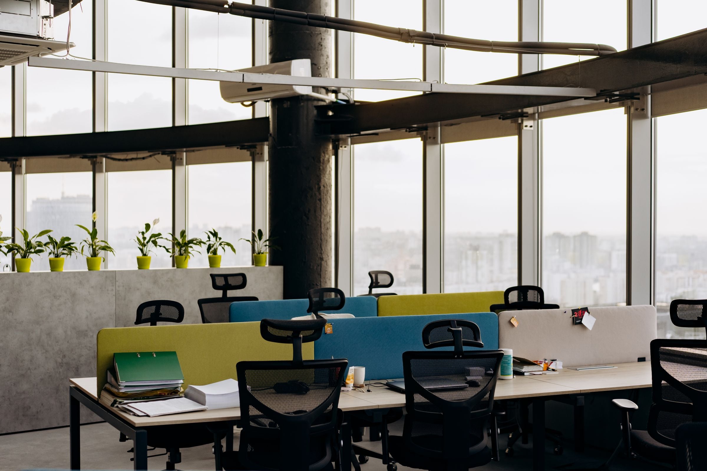 A spacious open office with colorful dividers, large windows, and a cityscape view, perfect for creative work environments.