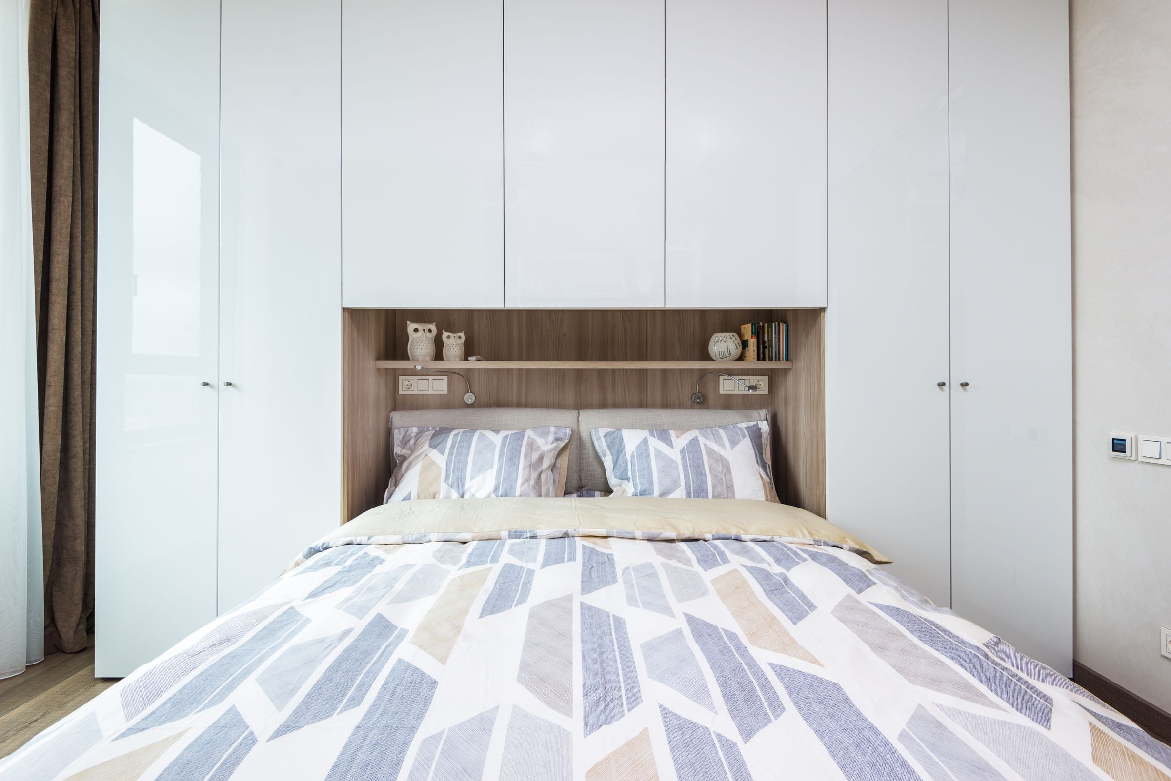 Interior of modern comfortable bedroom with bed with pillows and blanket under shelf combined with bedside wardrobe