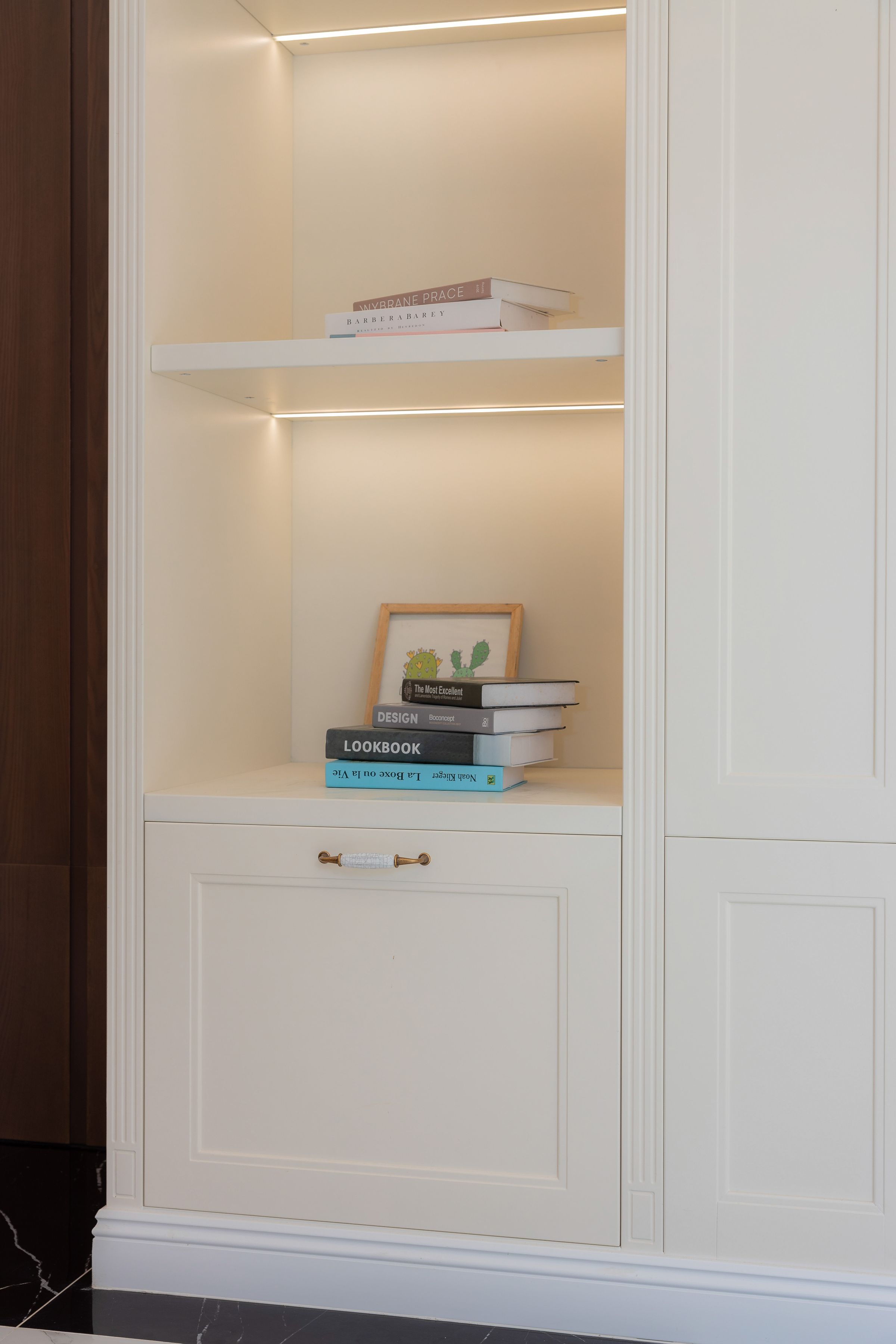 Stylish bookshelf with art and books, illuminated by subtle soft lighting in a minimalist room.